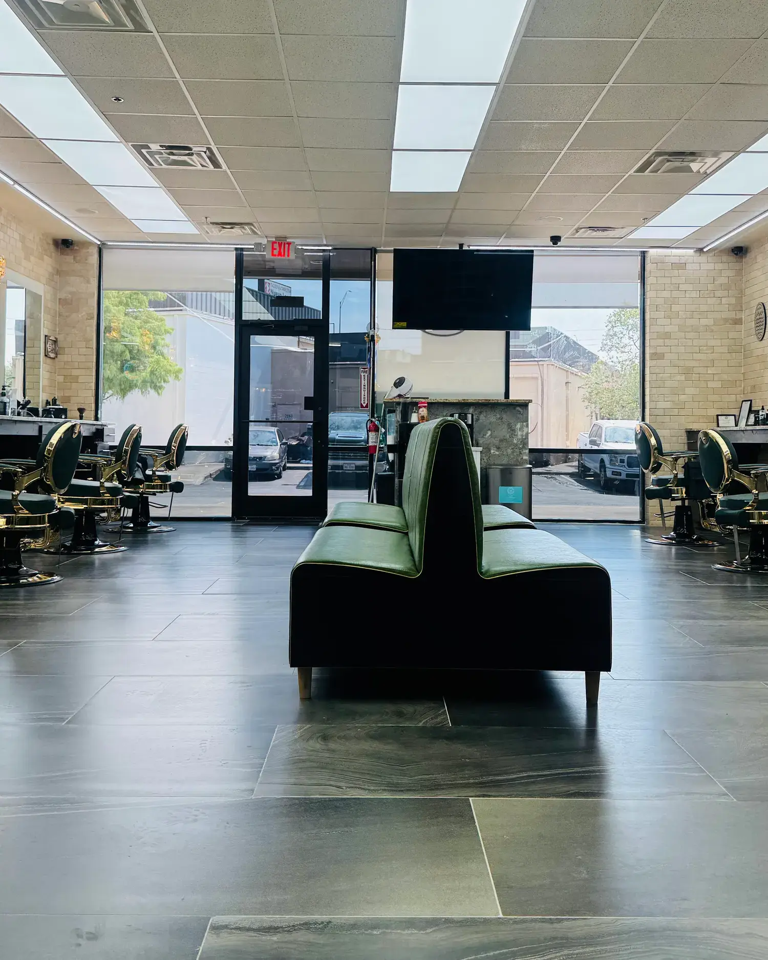 Inside KP's Barber Shop: green leather barber chairs with gold frames along both walls and a green waiting bench