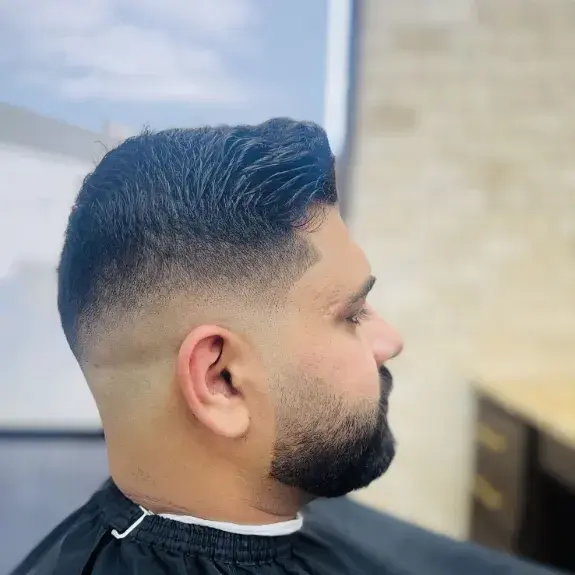 Skin fade with a combed top and a full beard